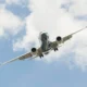 Airliner photographed from below with landing gear down flying overhead against a cloudy blue sky