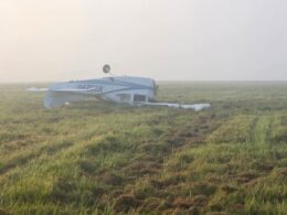 Small white airplane wreck on a grassy field upside down with a wing broken in a foggy morning