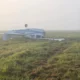 Small white airplane wreck on a grassy field upside down with a wing broken in a foggy morning
