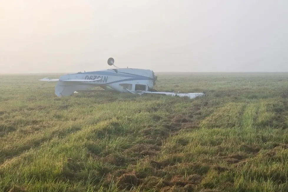 cessna 210 wreckage Small white airplane wreck on a grassy field upside down with a wing broken in a foggy morning