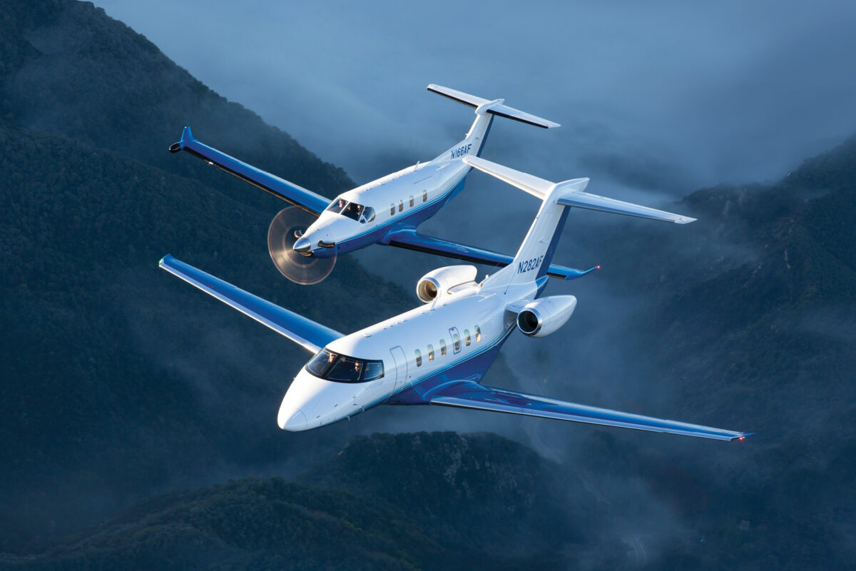 Two blue and white corporate jets fly in tight formation over misty green mountains