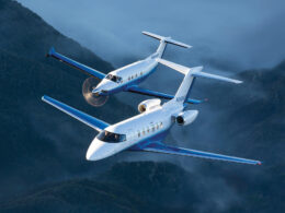Two blue and white corporate jets fly in tight formation over misty green mountains