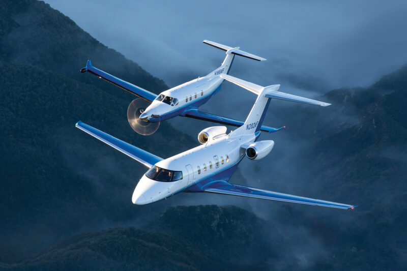 download Two blue and white corporate jets fly in tight formation over misty green mountains