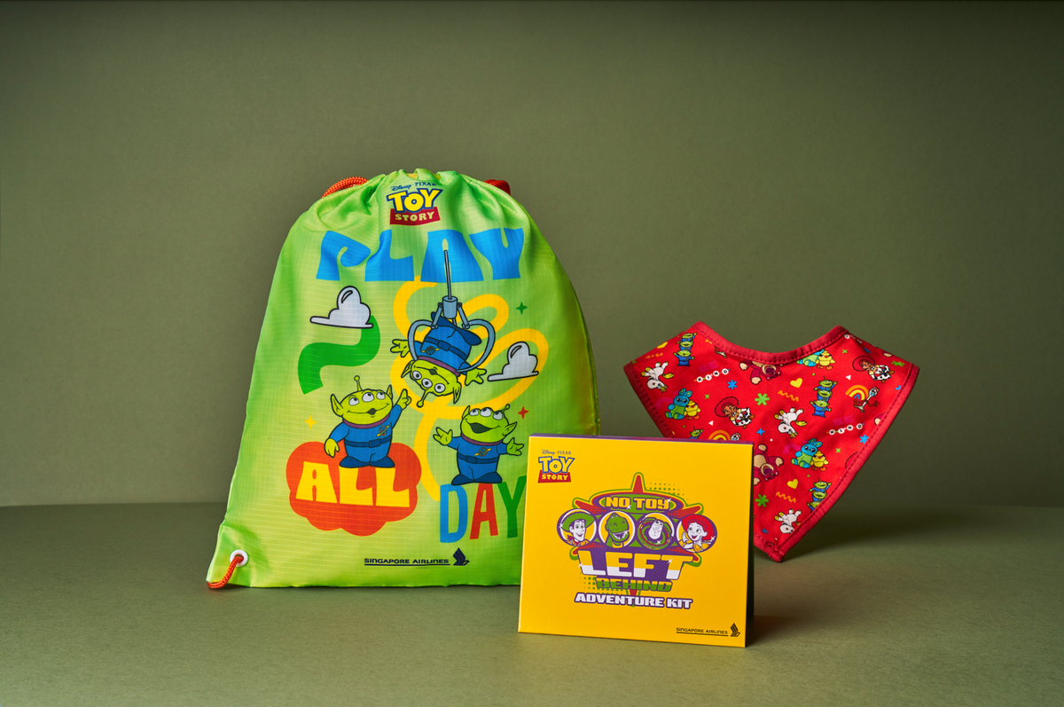 image Bright green Toy Story drawstring bag with Play Day artwork and cartoon aliens placed beside a yellow Left Behind Adventure Kit box and a red patterned fabric item in the background
