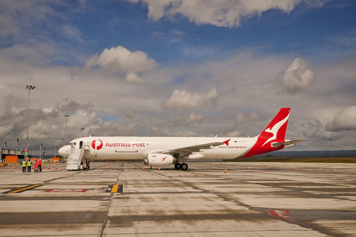 image Qantas freight airplane with Australia Post logo parked on a tarmac ground crew nearby under a cloudy sky