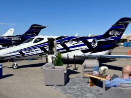 Private jet on a tarmac with its door open set up for a lounge area with couches and a man relaxing nearby
