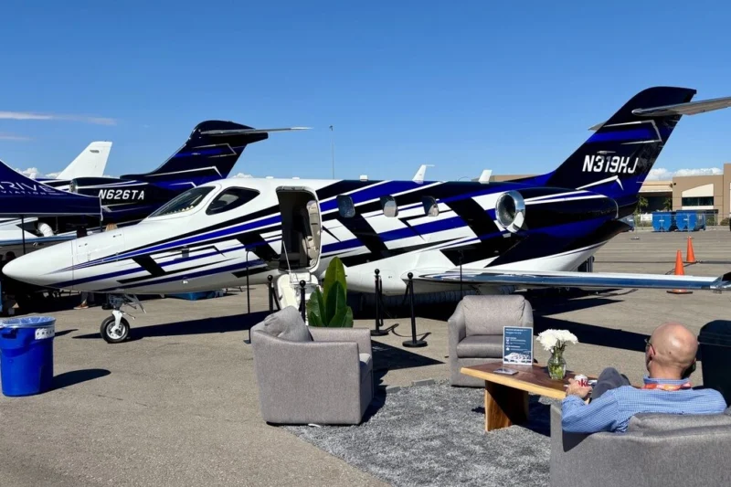 Private jet on a tarmac with its door open set up for a lounge area with couches and a man relaxing nearby