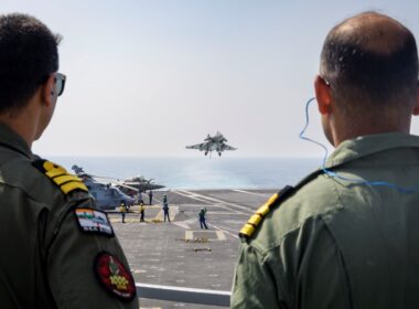 Two service members of the Indian Navy watch a Rafale fighter arrested landing on the Charles de Gaulle aircraft carrier