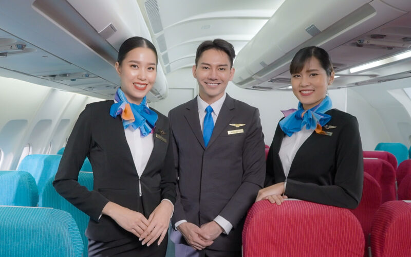 Portrait of three man and woman in blue suit flight attendant air hostess in economy class cabin smiling to welcome passenger at airplane.