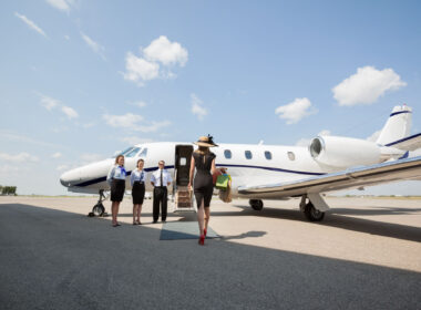 Rear view of rich woman walking towards private jet while pilot and stewardesses standing at airport terminal