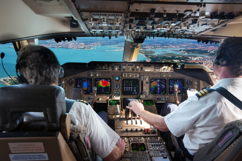The cockpit of modern jet airplane. Aircraft flies above the city landscape and river. Pilots at work.