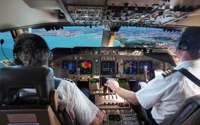 The cockpit of modern jet airplane. Aircraft flies above the city landscape and river. Pilots at work.