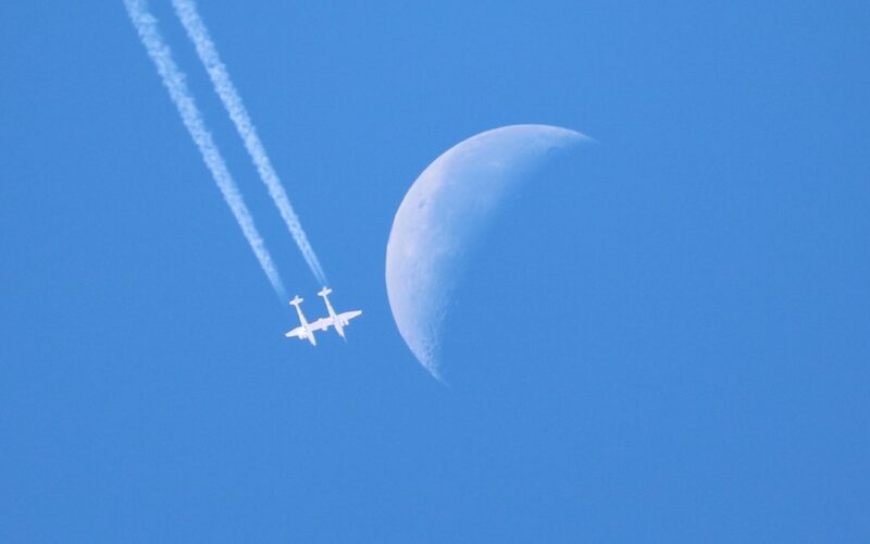 Virgin Galactic VMS Eve flies in a blue sky with the moon in the background
