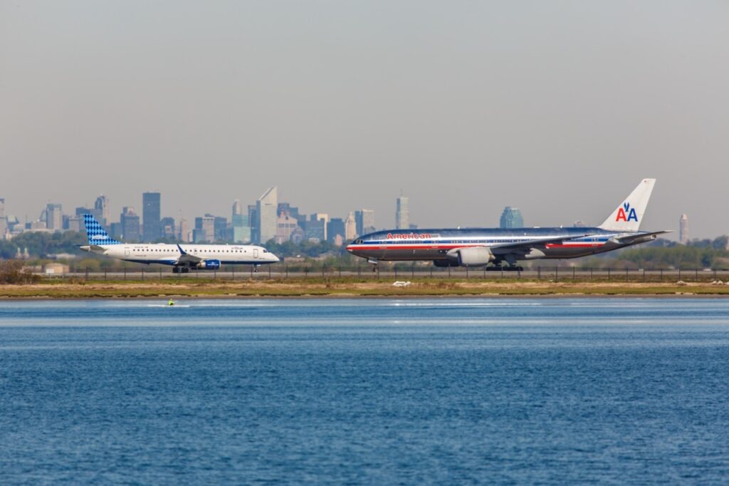 jet blue and american airlines planes standing on a runway next to a river